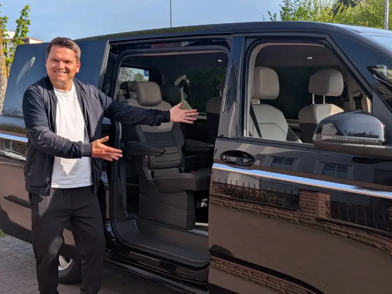 Friendly driver presenting spacious interior of modern black shuttle van with comfortable seating for passenger transportation service.