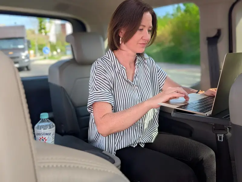 Woman working on laptop in backseat of shuttle vehicle during commute